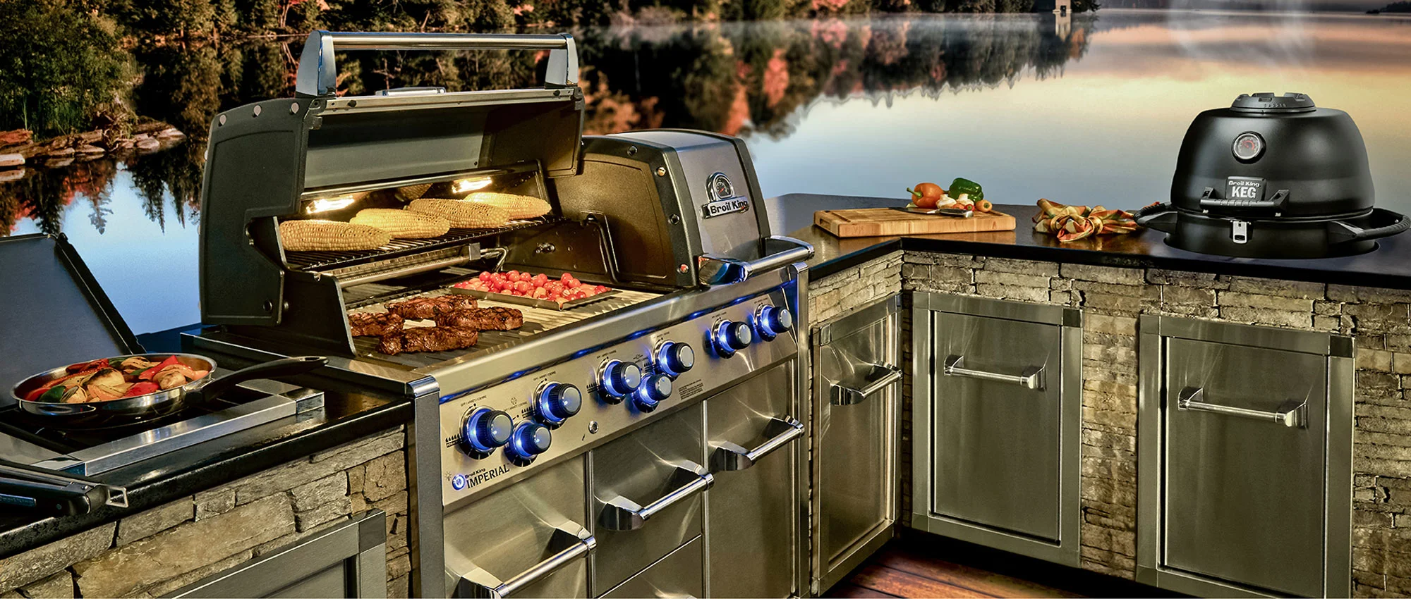 Broil King Imperial beépített gázgrill és KEG kamado kőborítású kültéri konyhában, tóparti naplementében